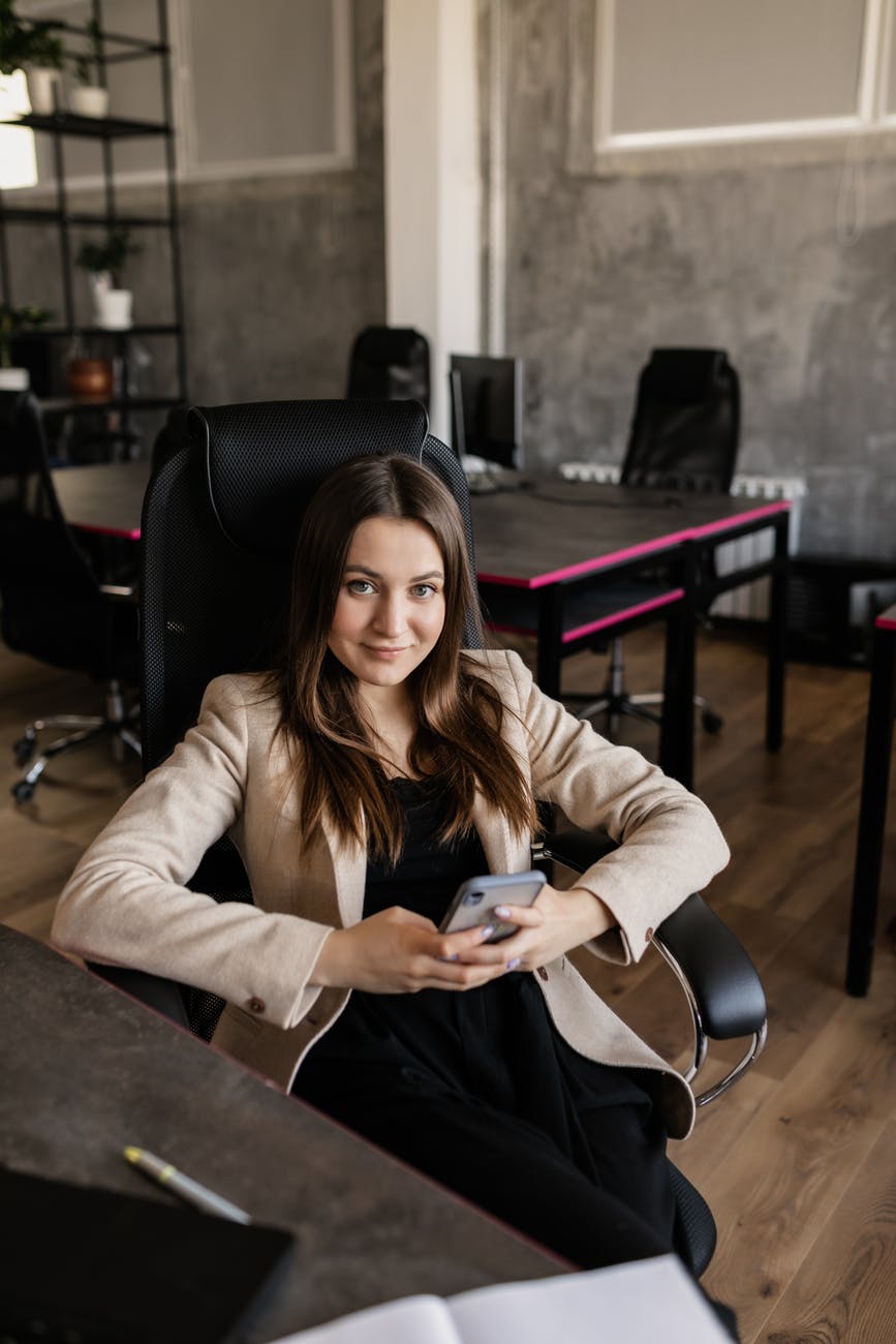 photo of a woman using her cell phone while sitting on a black chair